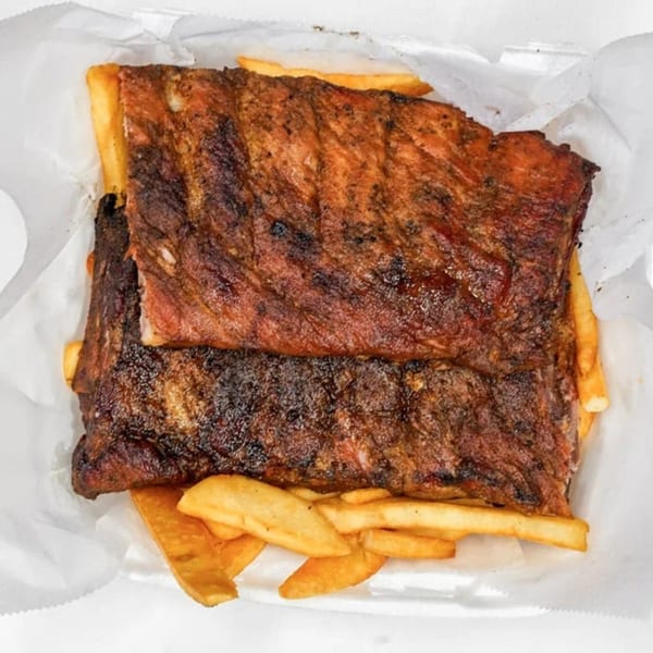 Two racks of Sunny's Bar B Que ribs with a side of golden french fries in a white paper container.