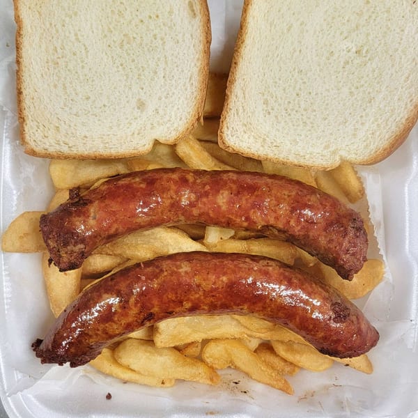 Two grilled sausages, a bed of fries, and two slices of white bread in a styrofoam container.