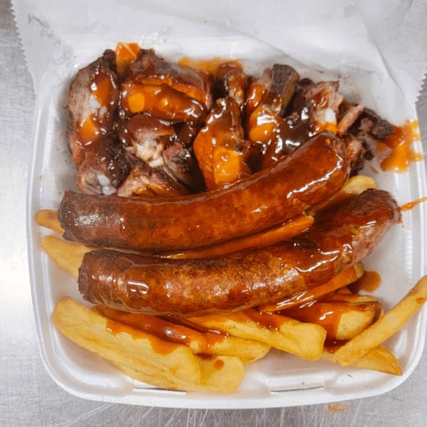 Sunny's Bar B Que plate with two sausages, chopped meat, and fries, all covered in BBQ sauce.