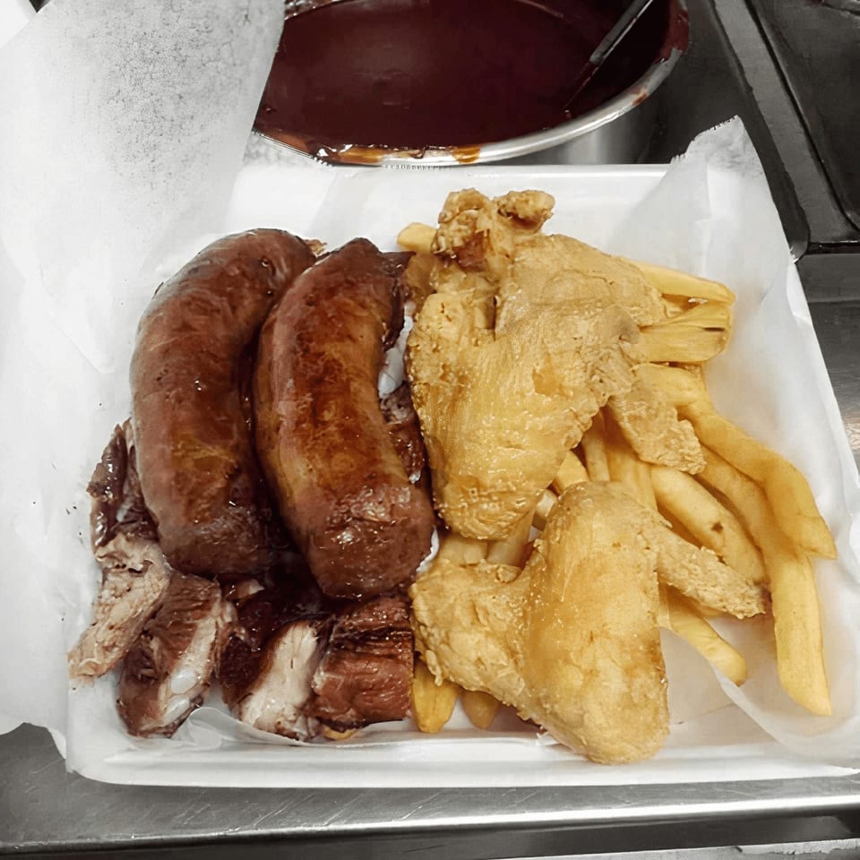 Sunny's Bar B Que platter with two sausages, sliced meat, fried chicken wings, and fries.