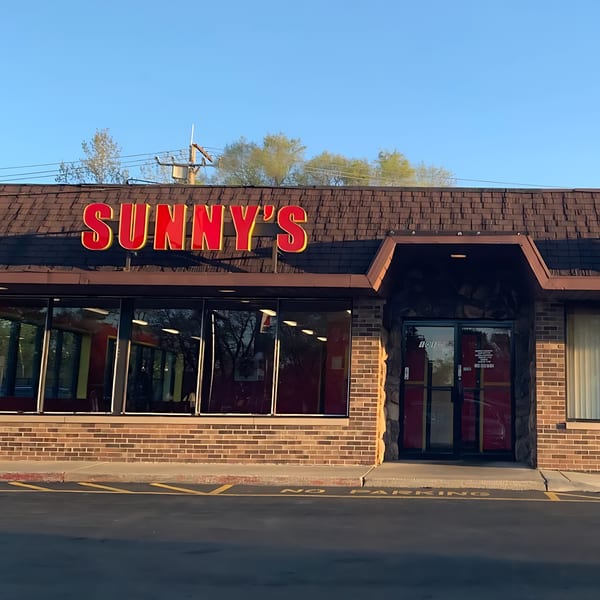 Sunny's Bar B Que restaurant exterior with a large red sign, brick facade, and glass windows.