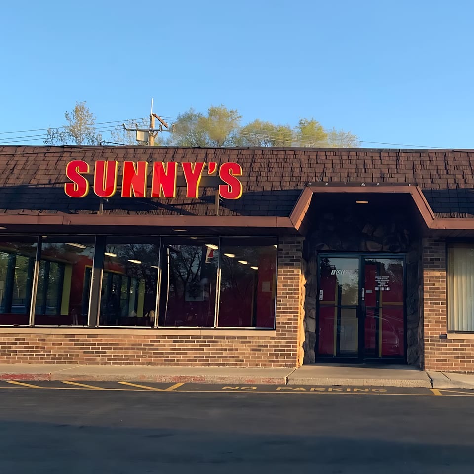 Sunny's Bar B Que restaurant exterior with a large red sign, brick facade, and glass windows.
